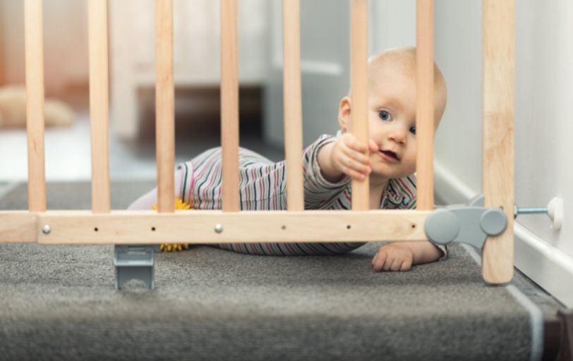 Baby liegt auf dem Bauch vor einem Treppenschutzgitter aus Holz