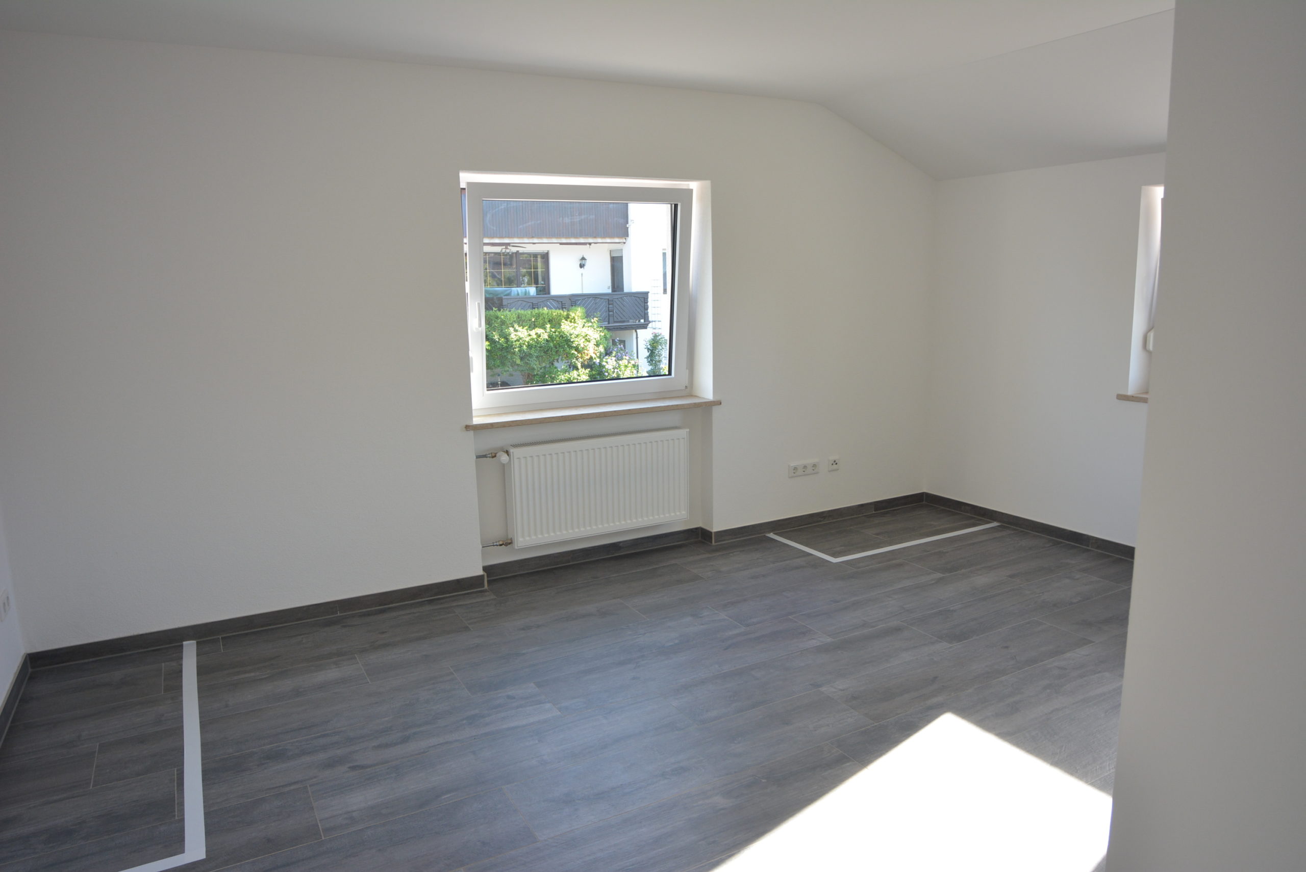 Weiß gestrichenes Zimmer mit zwei Fenstern und Bodenfliesen im Holzdekor