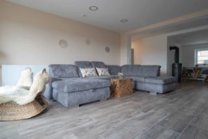 Wohnzimmer mit hellgrauem Lounge-Sofa und Bodenfliesen im Holzdekor